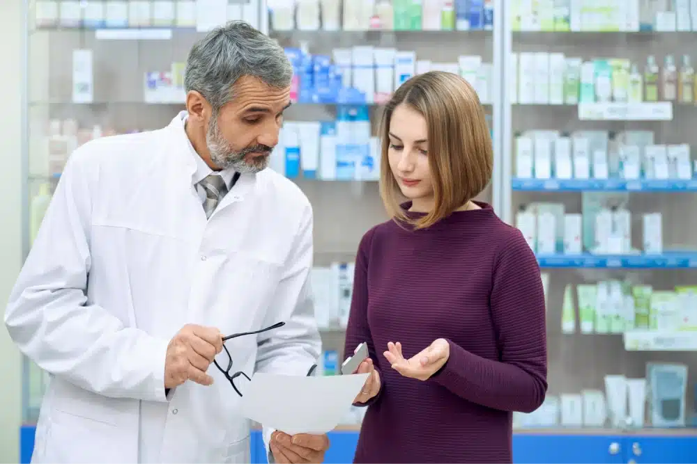 A pharmacist discusses medical history and prescription medications to a young woman.